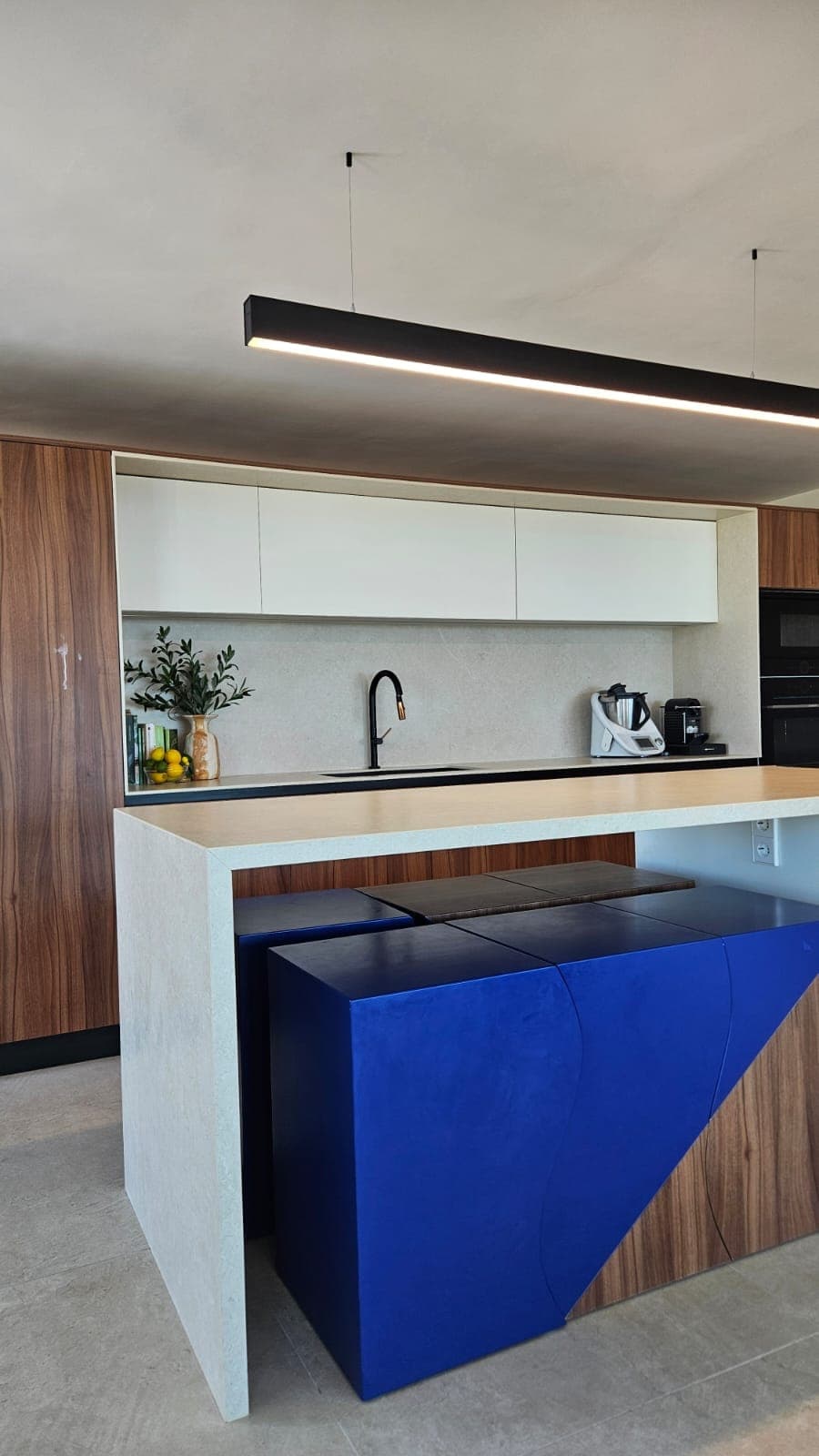 Sculptural stools under a kitchen island, blue and walnut geometry within the architecture
